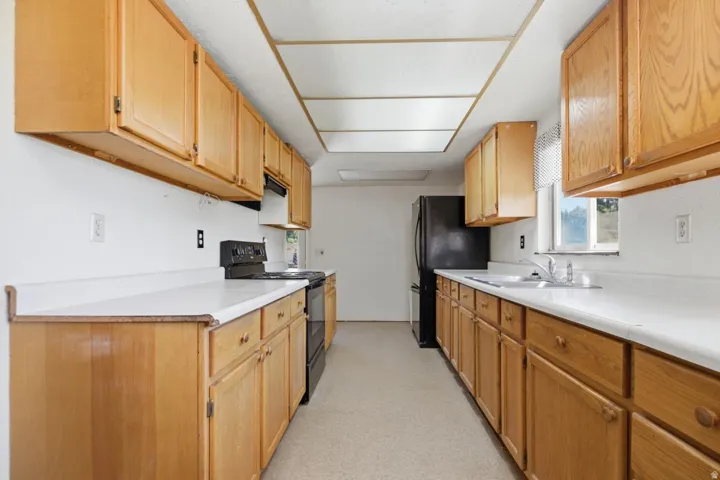 Galley kitchen featuring wood cabinetry, white countertops, a double basin sink, and a black range