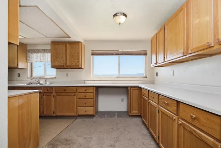 Kitchen featuring wood-finish cabinetry, white countertops, a stainless steel sink, and carpet flooring