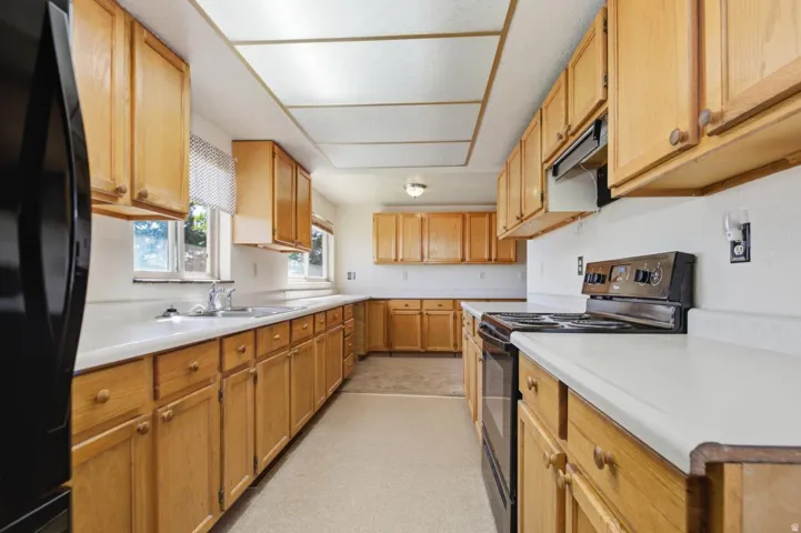 Galley kitchen with wood-finish cabinetry, white countertops, built-in double basin sink, and a four-burner electric range