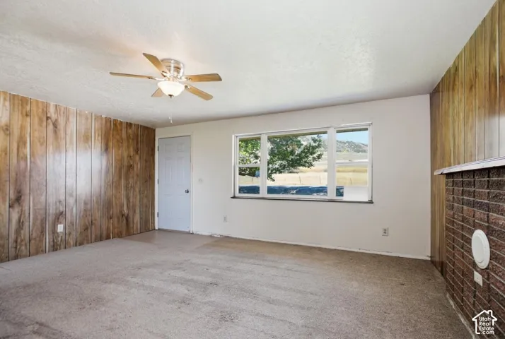 Interior space featuring wood-panel accent walls, a ceiling fan with integrated lighting, and a large window