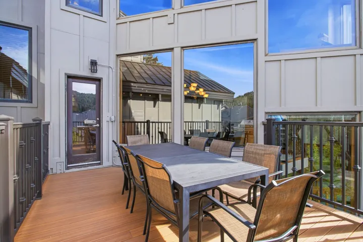 Expansive outdoor deck featuring wood-finish flooring, dark metal railings, and a full-light exterior door