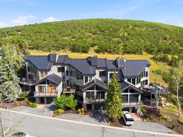 Multi-level exterior with a dark metal roof, multiple balconies, an attached garage, and surrounding mature trees