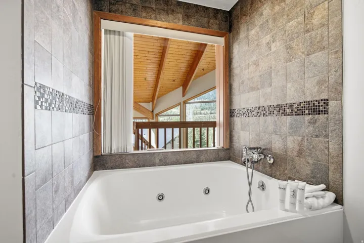 Jetted soaking tub with chrome fixtures, surrounded by large format wall tile with a mosaic accent band, and a wood-trimmed window