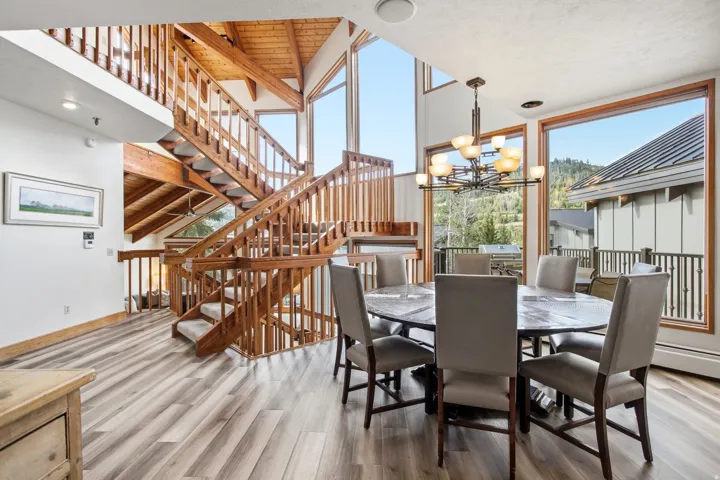 Expansive windows, wood-finish flooring, exposed wood beams, and a grand wooden staircase with carpeted treads