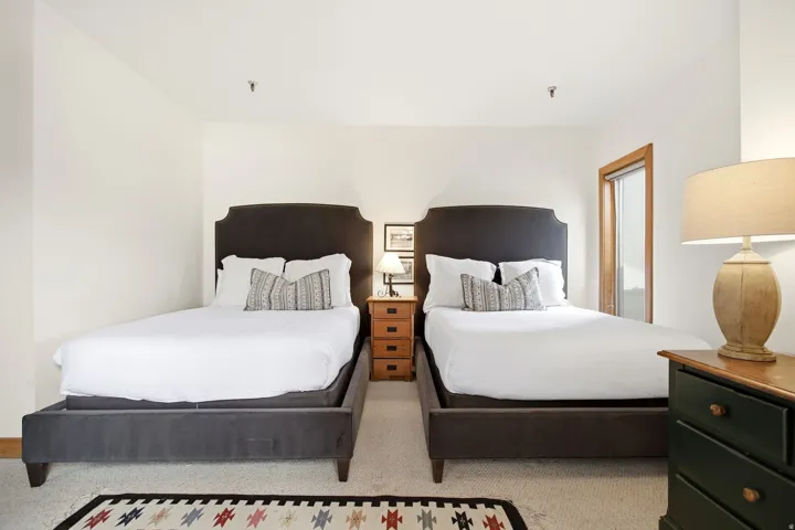 Two upholstered bed frames with decorative headboards, a three-drawer nightstand, and a light-toned wood door frame