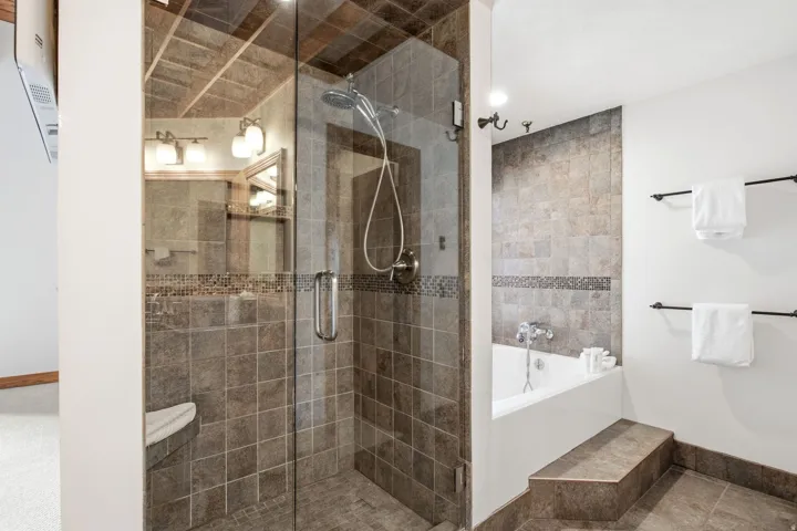 Glass-enclosed shower with a rain showerhead, mosaic tile accent band, and built-in shower seat