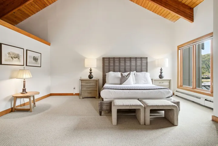 Vaulted ceilings with exposed wood beams, expansive window, light-toned carpeting, and wood-toned trim