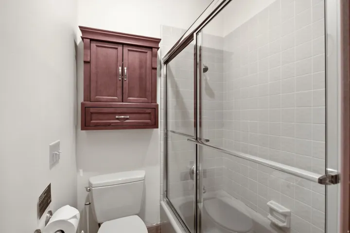Built-in wall cabinet with drawer, toilet, and tiled shower with sliding glass enclosure