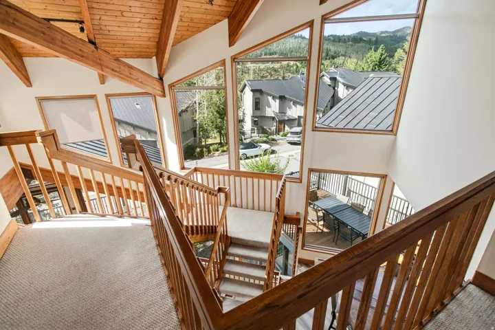 Vaulted wood-paneled ceiling with exposed beams, wood-framed windows, wood staircase with carpeted treads, exterior balcony, and mountain scenery