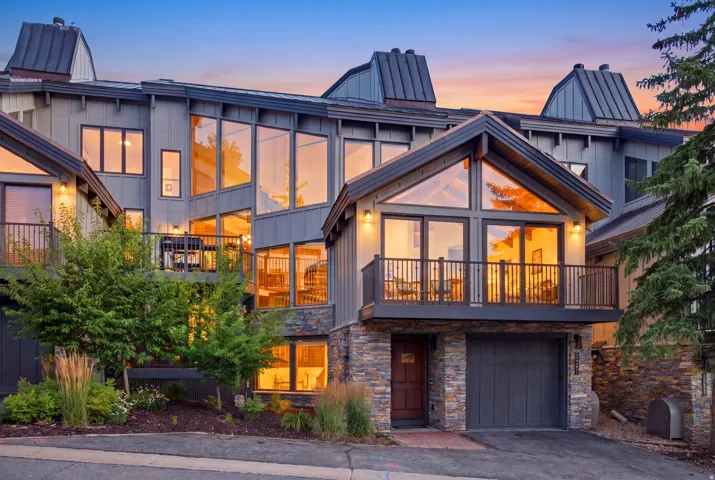 Multi-level exterior with extensive glazing, board and batten siding, stone veneer accents, multiple balconies with metal railings, and a prominent peaked roofline
