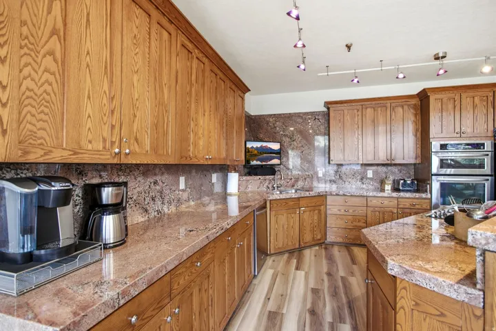 Wood-finish cabinetry, stone slab countertops, stone slab backsplash, integrated double ovens, and wood-finish flooring