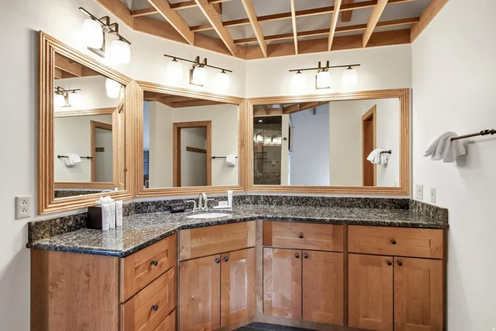 Custom vanity featuring wood cabinetry with dark hardware, a corner-mounted sink, and a speckled countertop