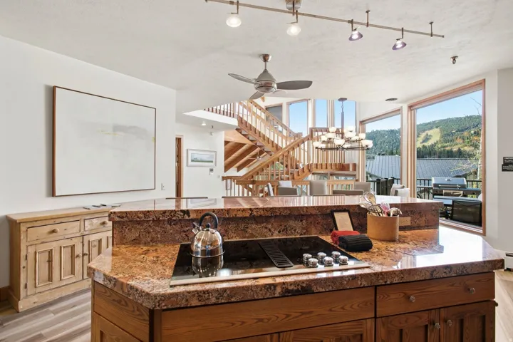Kitchen island with a built-in cooktop, stone countertop, and wood-finish cabinetry