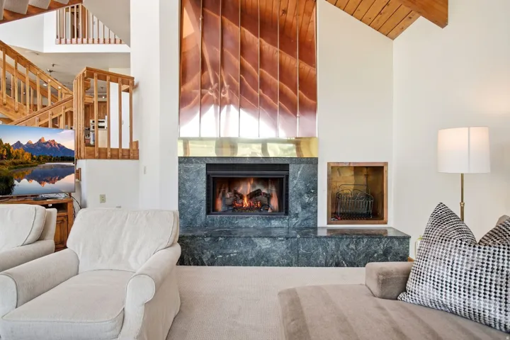 Fireplace with a stone surround, wood-paneled ceiling, exposed wood beams, and a multi-level wooden staircase