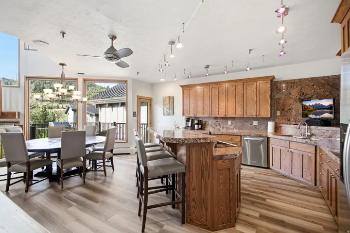 Kitchen and dining area featuring wood-finish flooring, wood cabinetry, stone countertops, stainless steel appliances, and a ceiling fan