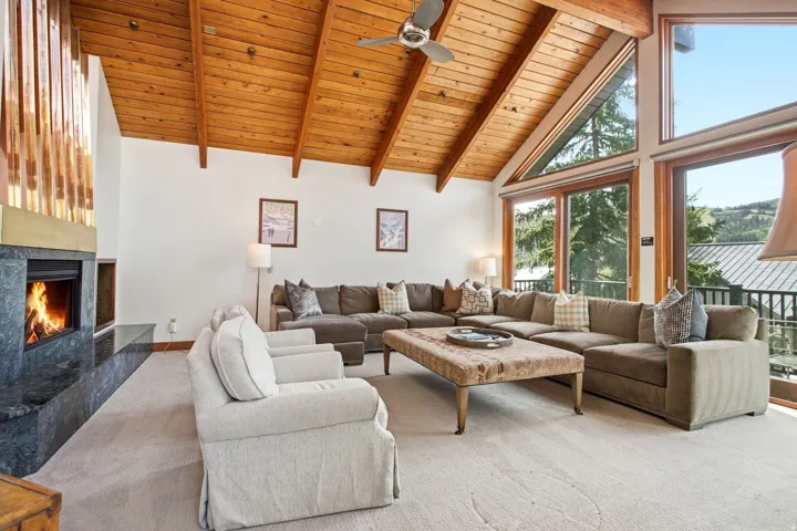 Vaulted wood-paneled ceiling with exposed beams, large windows, ceiling fan, built-in fireplace with stone surround