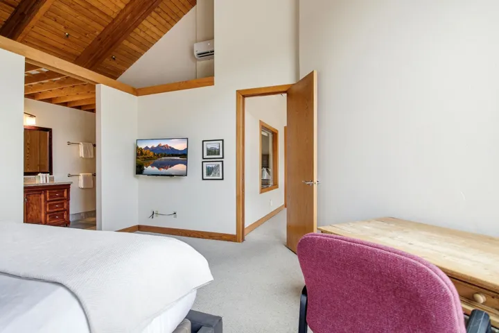 Vaulted wood-plank ceiling with exposed beams, wood-trimmed doorways, and a wall-mounted climate control unit