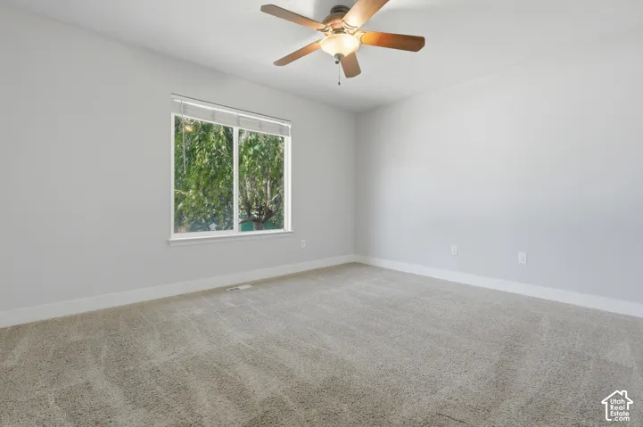 Neutral gray wall finishes, light-toned carpeting, ceiling fan with integrated lighting, and a large window overlooking natural scenery