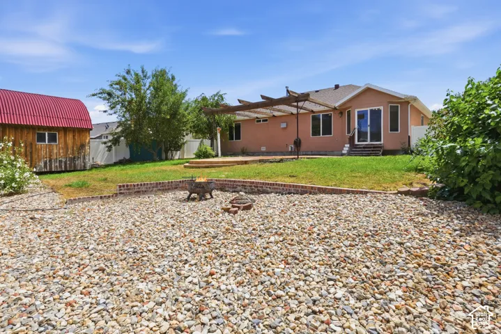 Expansive backyard featuring a gravel patio, a brick retaining wall, a wood pergola, and a detached shed with a red metal roof
