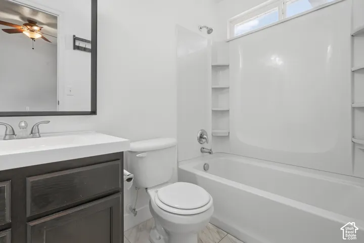 White vanity countertop, dark wood-finish vanity with drawer storage, framed mirror, white tub and shower surround with integrated shelving, and a window for natural light