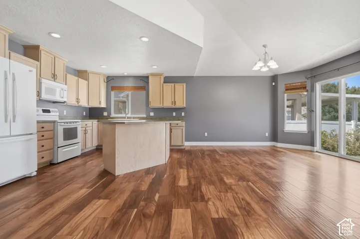Kitchen featuring wood-finish flooring, light-toned cabinetry, a central island, and white appliances
