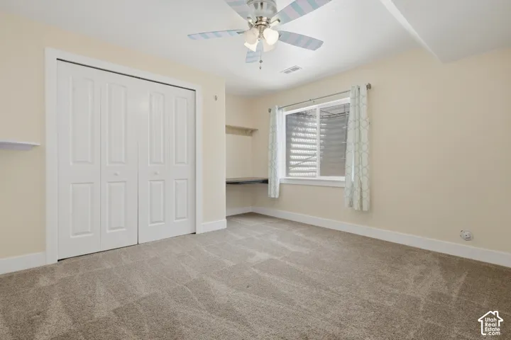 Wall-to-wall carpeting, bi-fold closet doors, built-in desk, window with blinds, and ceiling fan