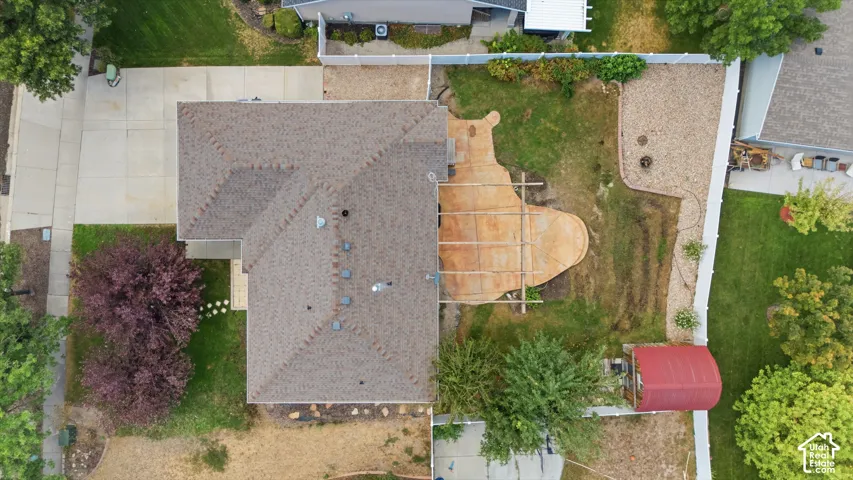 Expansive property featuring a concrete driveway, asphalt shingle roof, a large concrete patio, and a separate storage structure
