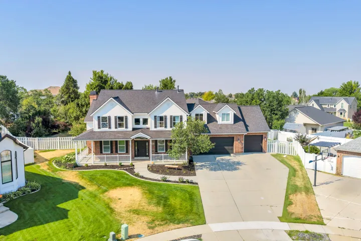 Two-story residence featuring a brick facade with white siding and dark shutters, a covered front porch, a two-car garage, and a concrete driveway