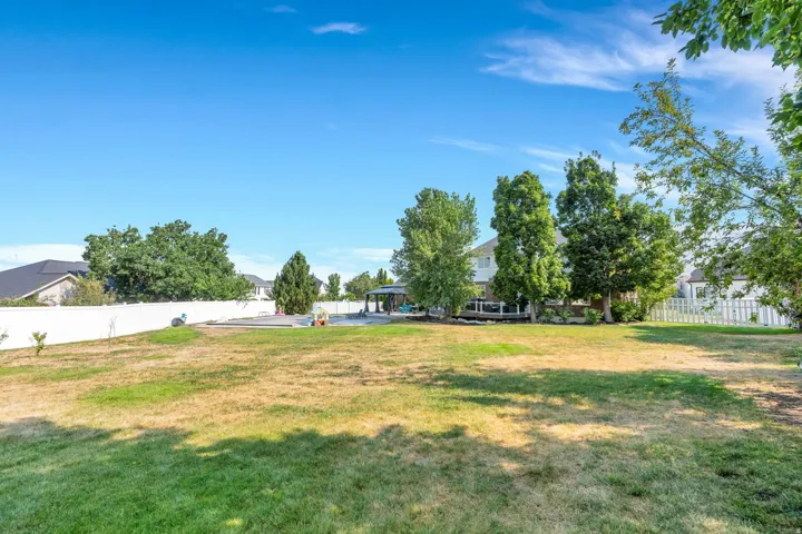 Expansive backyard with a large lawn area, mature trees, white privacy fencing, and a separate white picket fence