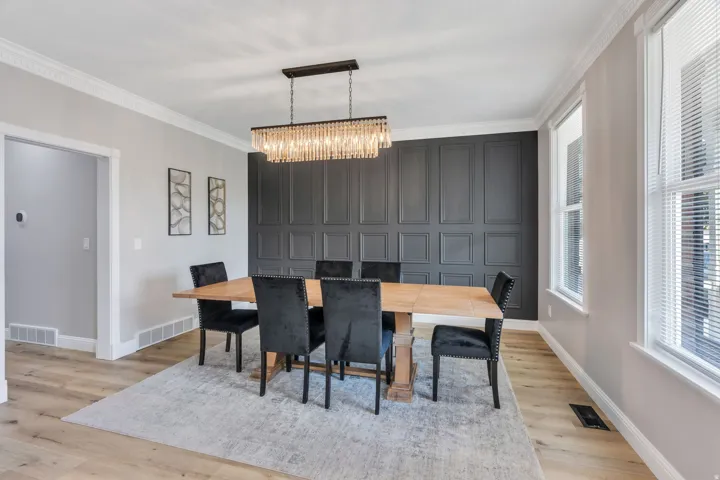 Decorative wainscoting accent wall, wood-finish flooring, crown molding, and a crystal chandelier