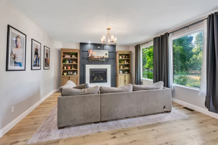 Living area featuring wood-finish flooring, a central fireplace with shiplap detailing, built-in shelving, a chandelier, and multiple windows