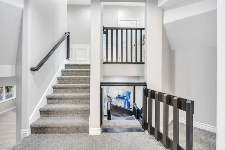 Staircase featuring carpeted treads, a dark handrail, and white wainscoting