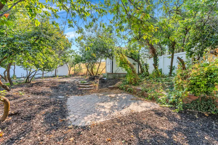 Terraced backyard with mature trees, a patterned paver patio, and a privacy fence
