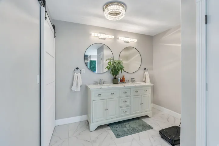 Dual vanity with integrated sinks, two circular mirrors, and overhead lighting fixtures