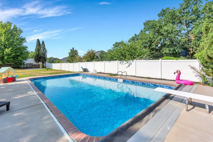 In-ground swimming pool with a diving board, concrete surround, and privacy fencing