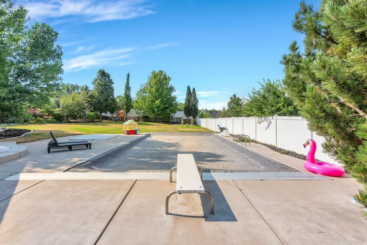 Concrete patio surrounding a covered swimming pool with a diving board, expansive lawn, and mature landscaping