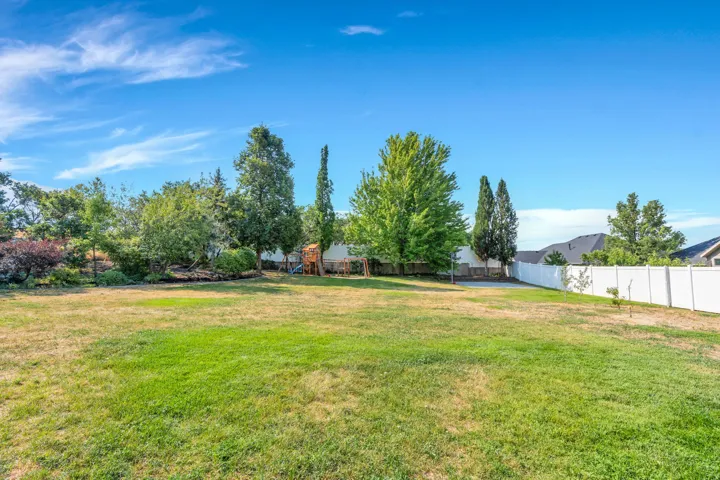 Expansive lawn with mature trees and a white privacy fence