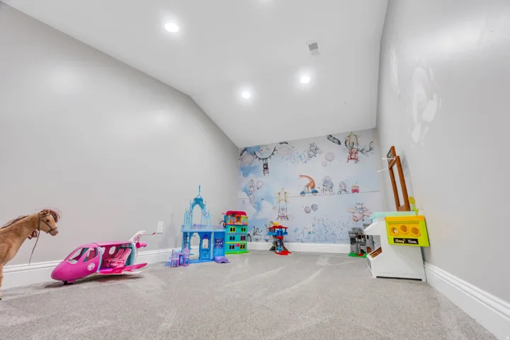 Recessed lighting illuminates a spacious room featuring sloped ceilings and light grey carpeting
