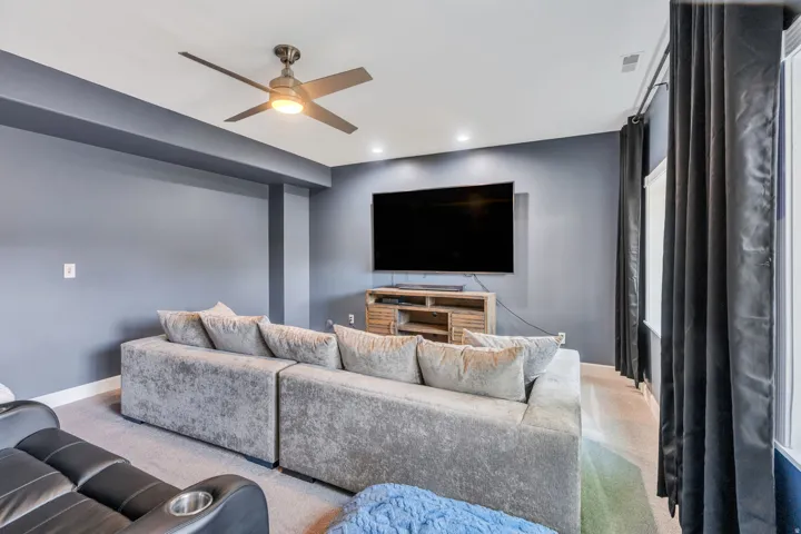 Recessed lighting, ceiling fan, dark-toned walls, and a mounted media console