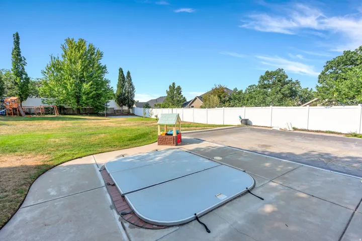 Expansive backyard featuring a large concrete patio, integrated spa with cover, manicured lawn, and privacy fencing