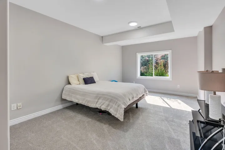 Recessed ceiling lighting, tray ceiling detail, large window, soft gray wall paint, and gray carpet