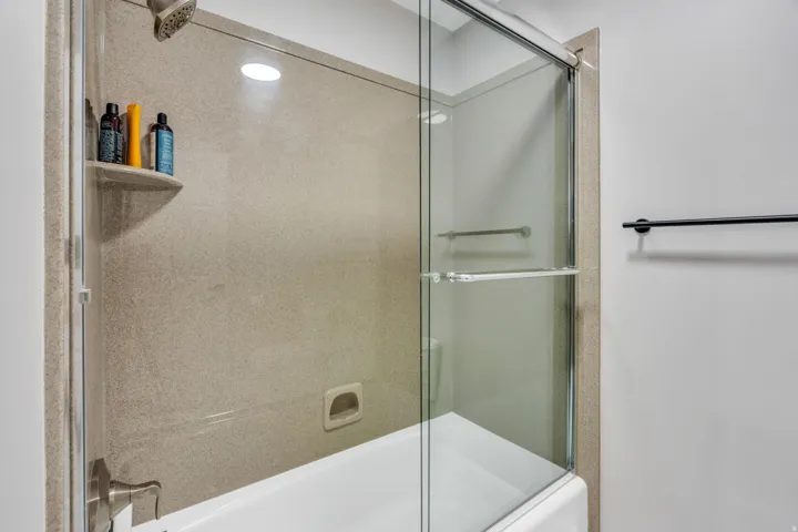 Bathtub with a glass sliding shower door, shower wall paneling, and an integrated corner shelf
