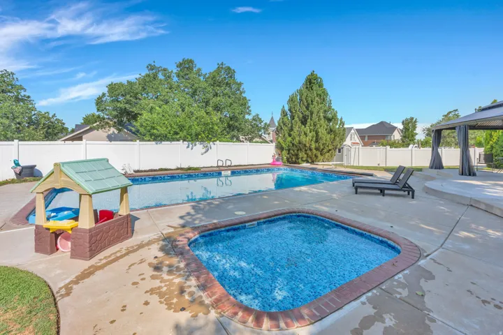 Inground swimming pool with an integrated spa, expansive concrete patio, and a privacy fence
