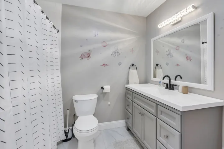 Single vanity with a white countertop and integrated sink, framed mirror, and a wall-mounted light fixture