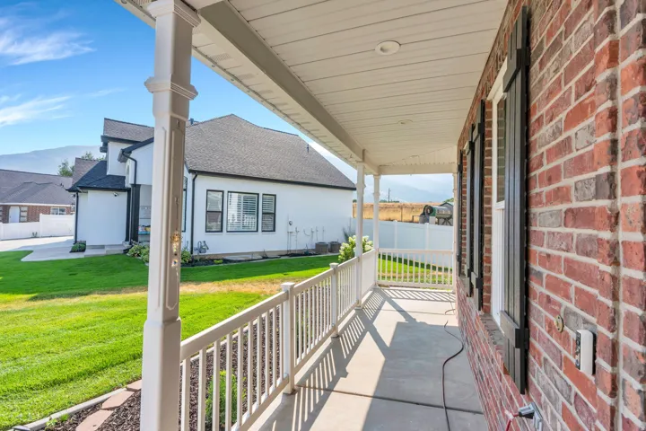 Brick exterior with black shutters and white trim, covered front porch, white railing, and a manicured lawn