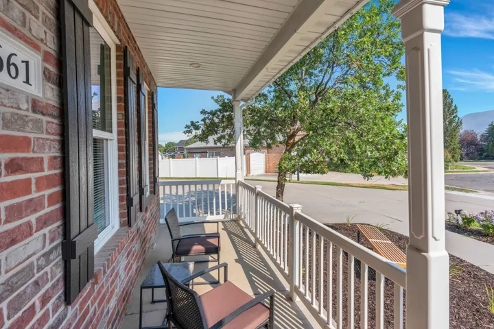 Brick exterior with dark shutters, covered front porch, white railing, and decorative column