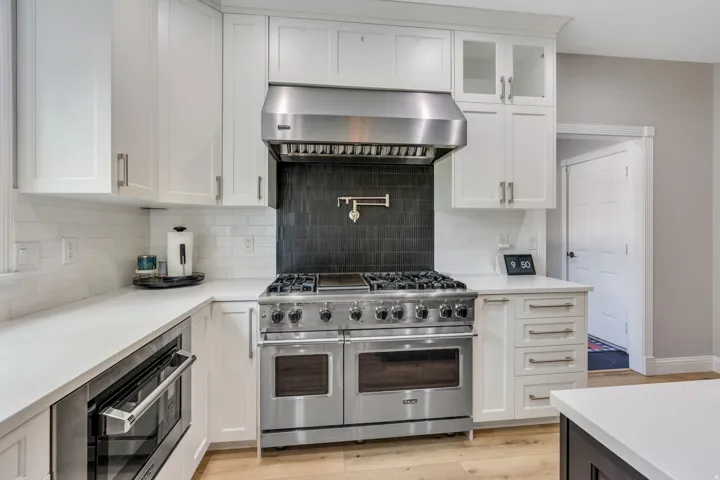 Stainless steel range with a pot filler, a built-in microwave, white shaker-style cabinetry, white subway tile backsplash, and light wood-finish flooring
