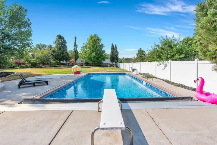 Expansive backyard featuring a rectangular swimming pool, concrete pool deck, diving board, and a white privacy fence