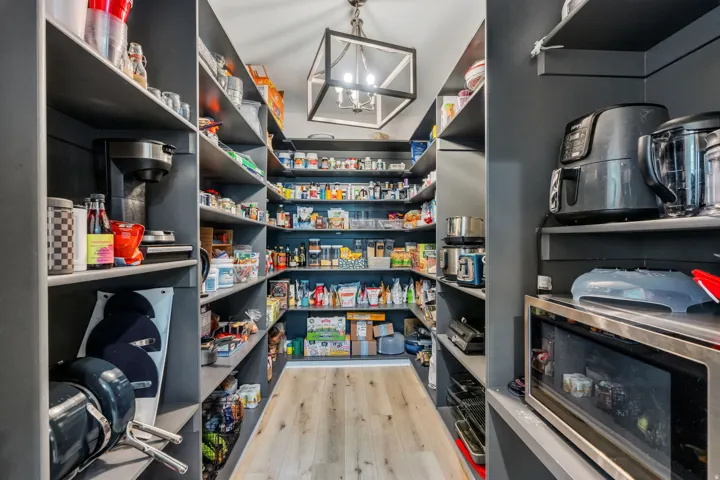 Walk-in pantry with extensive built-in shelving, wood-finish flooring, and a central ceiling light fixture