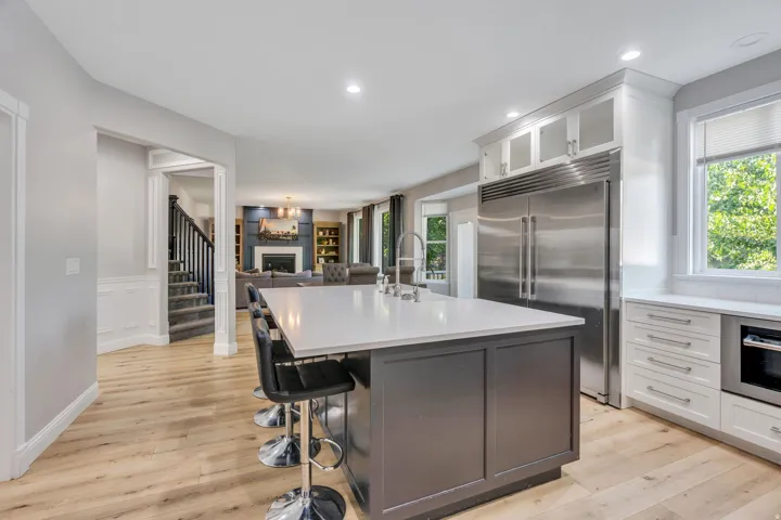 Kitchen featuring a large center island with a white countertop, stainless steel refrigerator, white cabinetry, and wood-finish flooring